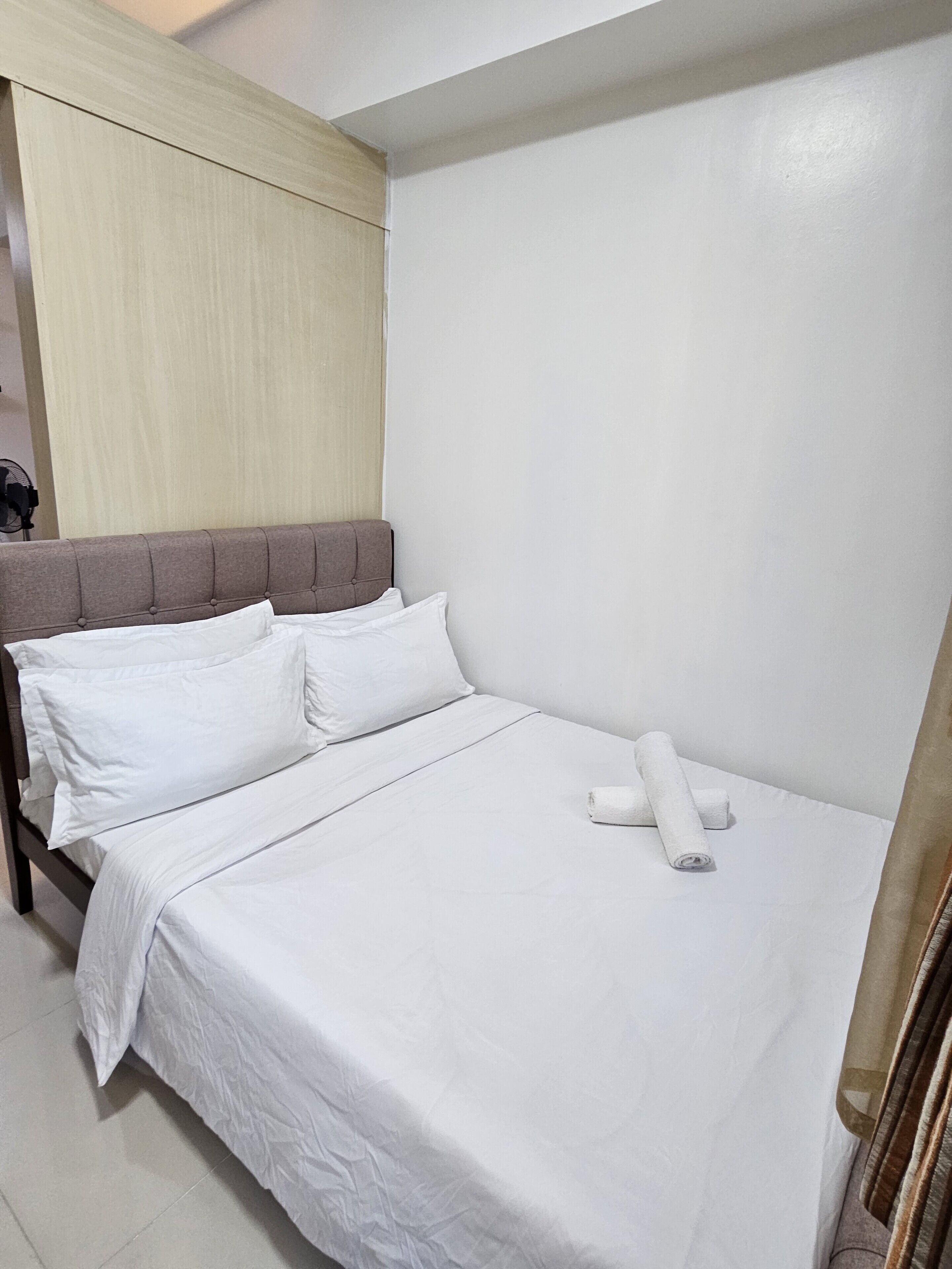 A neatly made bed with white linens, a wooden headboard, and a rolled towel on the footboard.