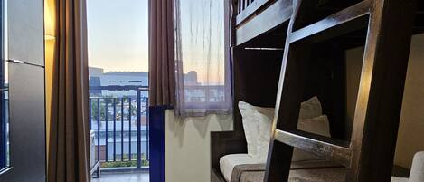 Habitación de hotel compacta con literas, un escritorio pequeño, una ventana con cortinas y un equipo de aire acondicionado.