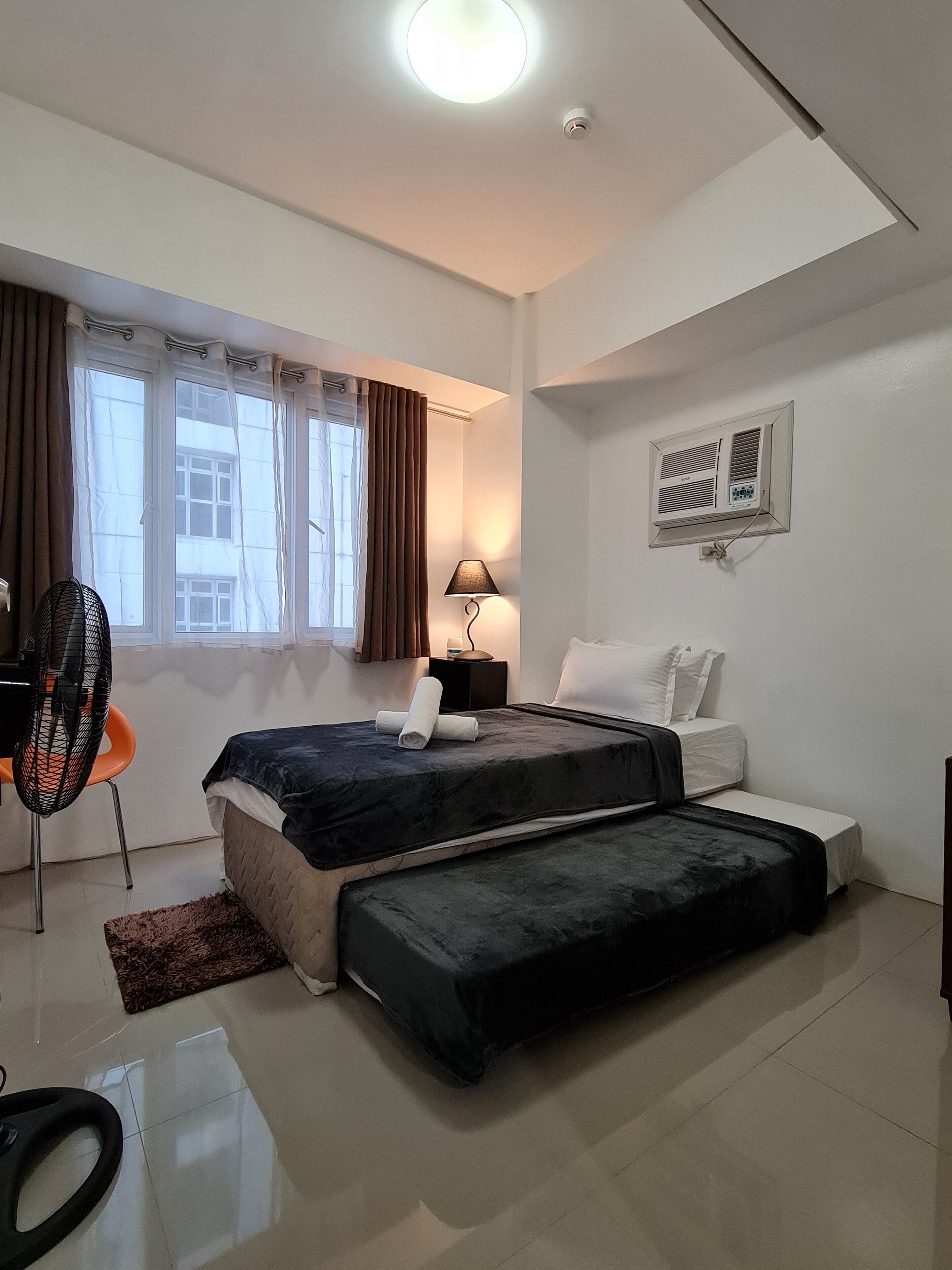 Un dormitorio con dos camas, un escritorio, una silla, una lámpara y un ventanal con cortinas.