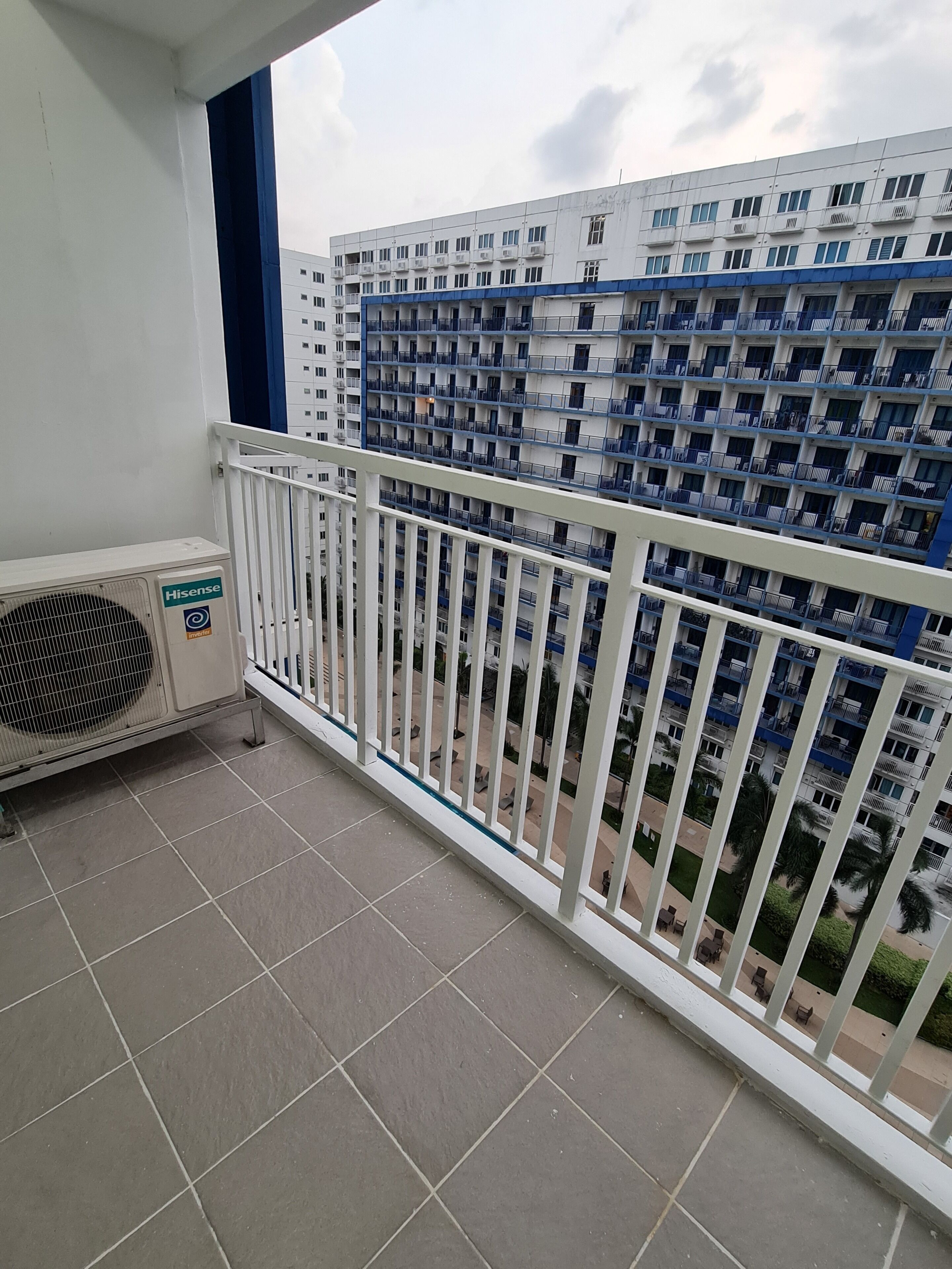 A balcony with a white railing, a Hisense air conditioner, and a view of a multi-story building with balconies.