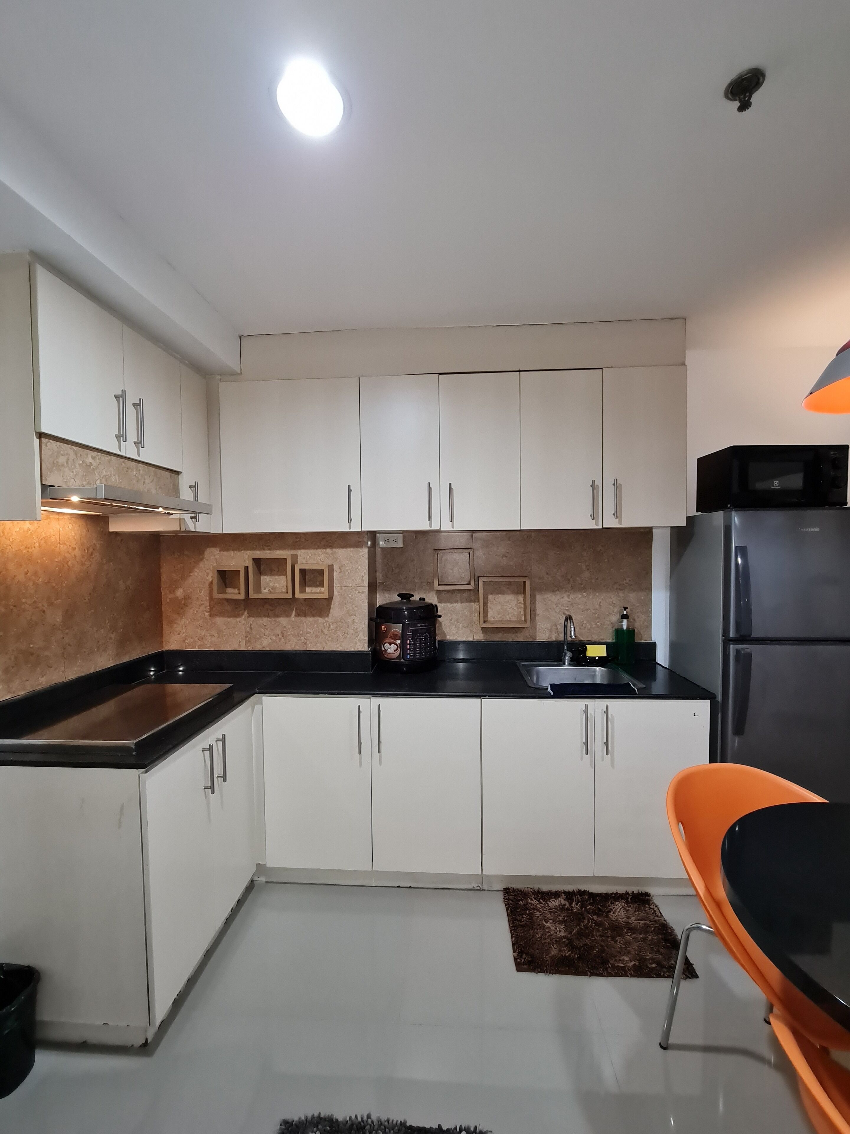 A modern kitchen with white cabinets, a black countertop, a built-in microwave, and a refrigerator.