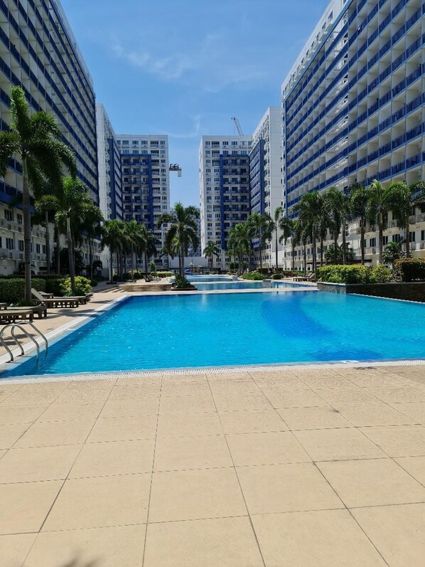 A swimming pool surrounded by high-rise buildings, palm trees, and a clear sky.