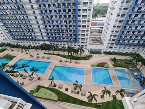 A high-rise hotel with multiple balconies, a central pool area with sun loungers, and surrounding greenery.