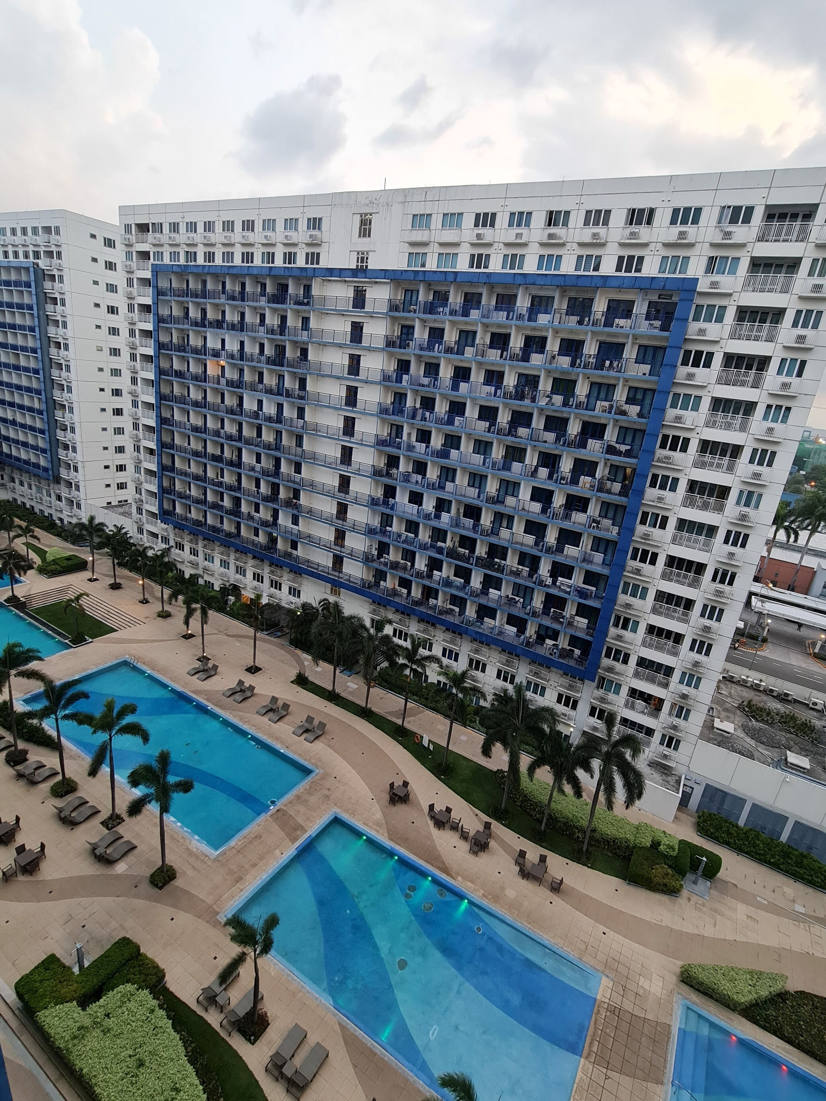 A high-rise hotel with multiple balconies, a swimming pool area with lounge chairs, and palm trees.