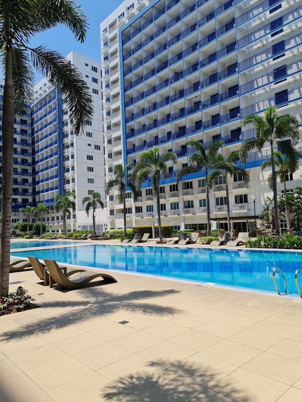 A hotel with multiple floors, a swimming pool, and palm trees.