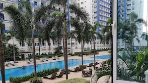 A hotel pool area with palm trees, lounge chairs, and a view of high-rise buildings. - Sea Residences - Condo R Us (Pasay)
