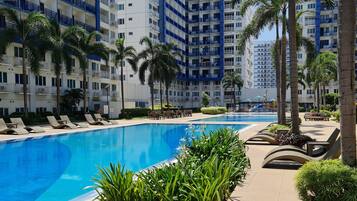 Una piscina con sillas de descanso y palmeras, rodeada de edificios altos.
