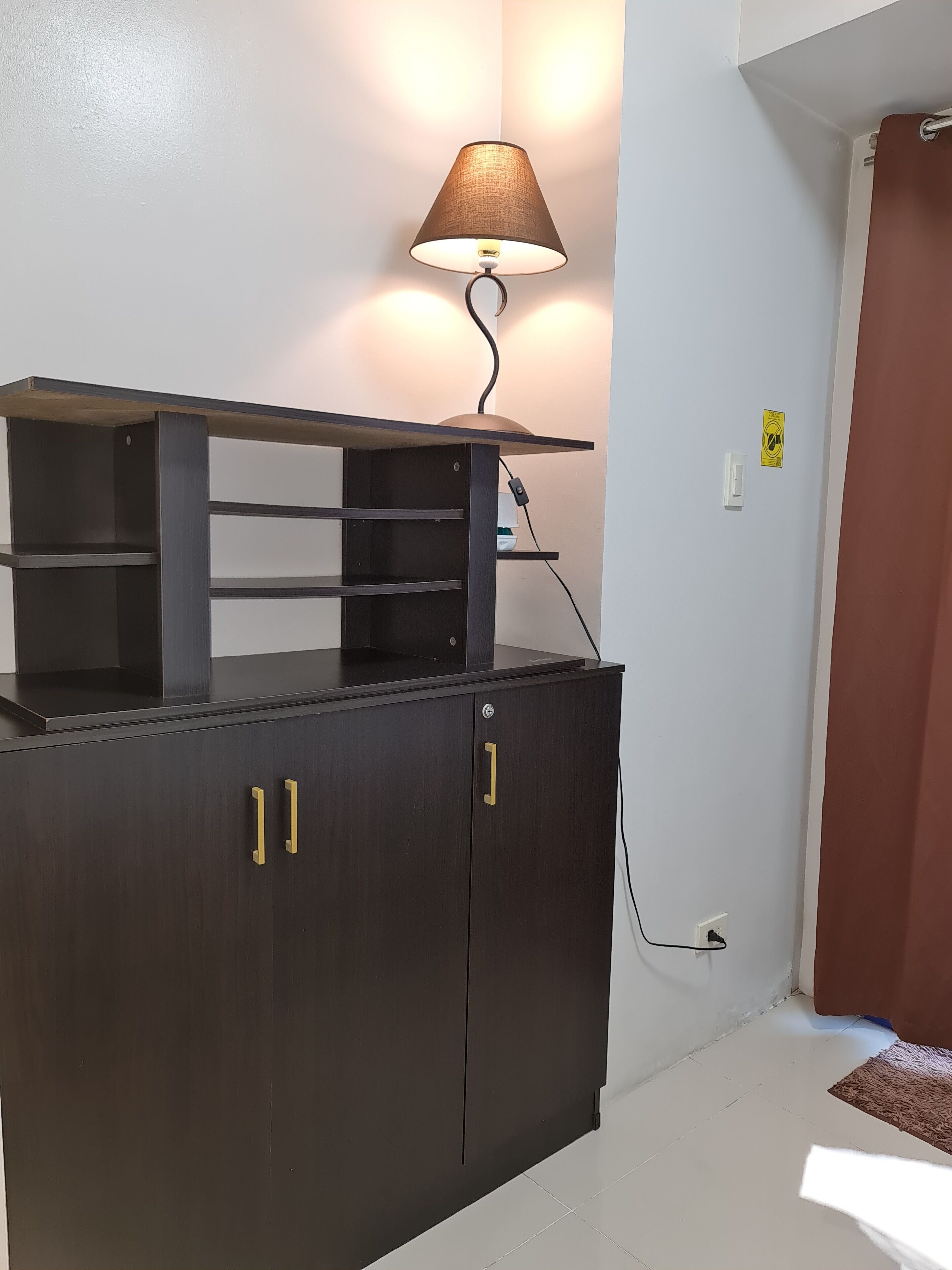 A dark wooden cabinet with two gold handles and a shelf on top.
