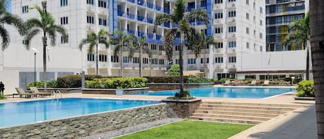 A modern hotel with a pool area, palm trees, and a well-maintained lawn.