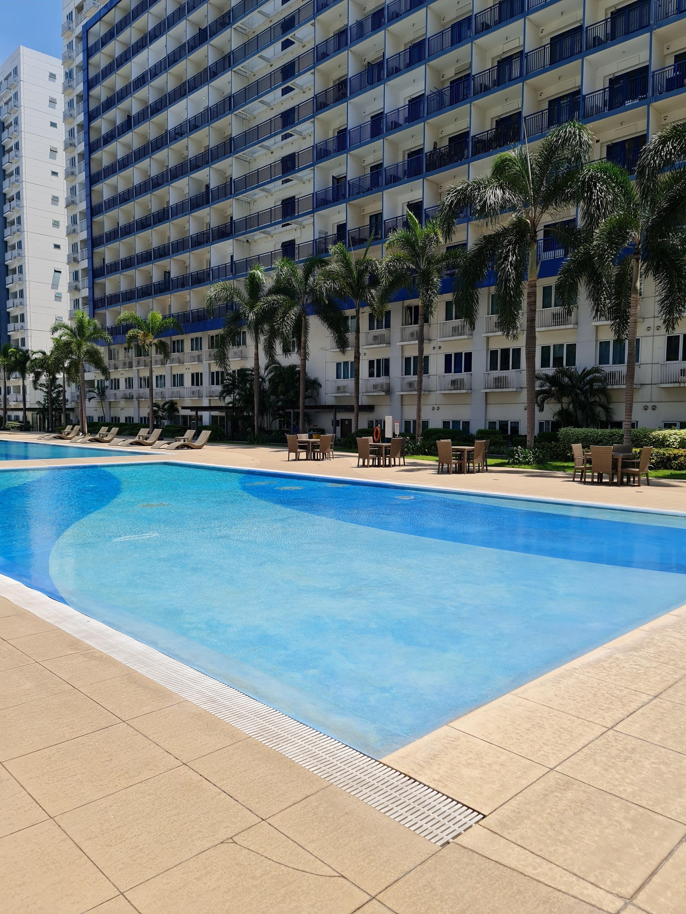 A swimming pool with lounge chairs and palm trees, surrounded by a high-rise building with balconies.