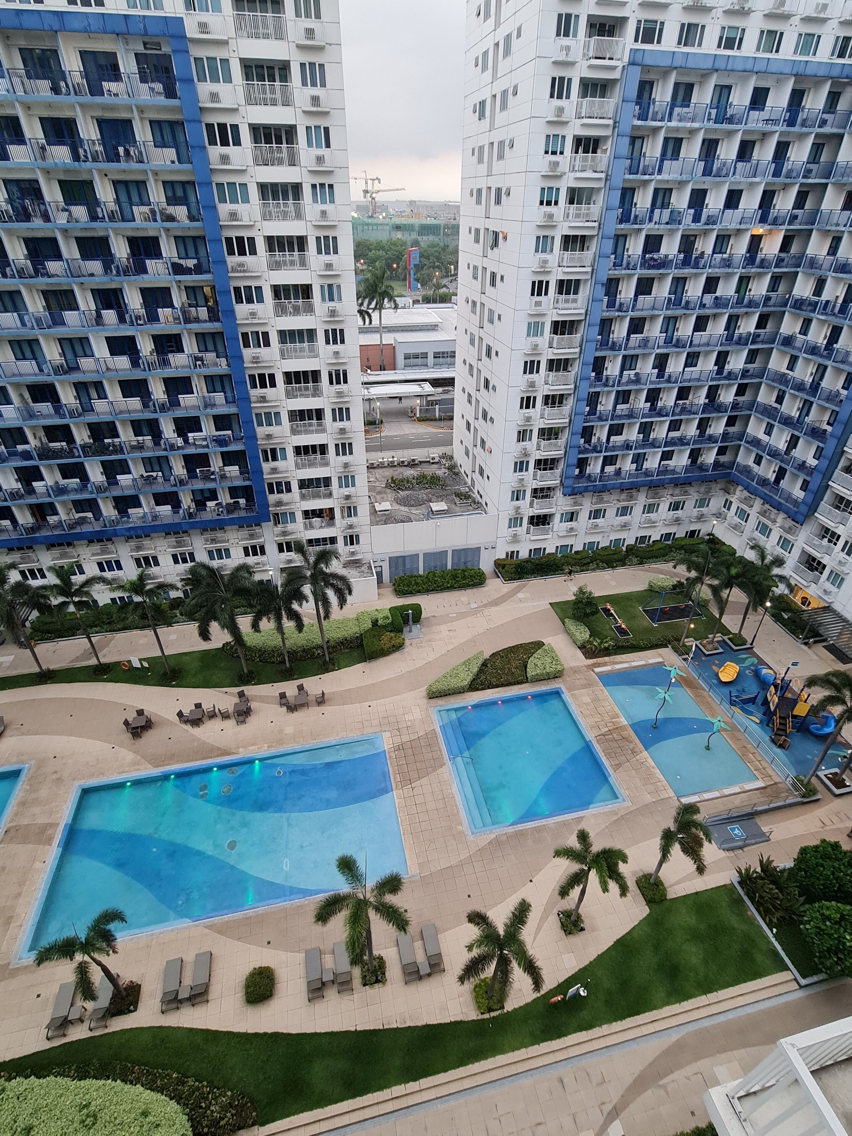 A high-rise residential building with multiple balconies, a central courtyard with a swimming pool, and surrounding greenery.