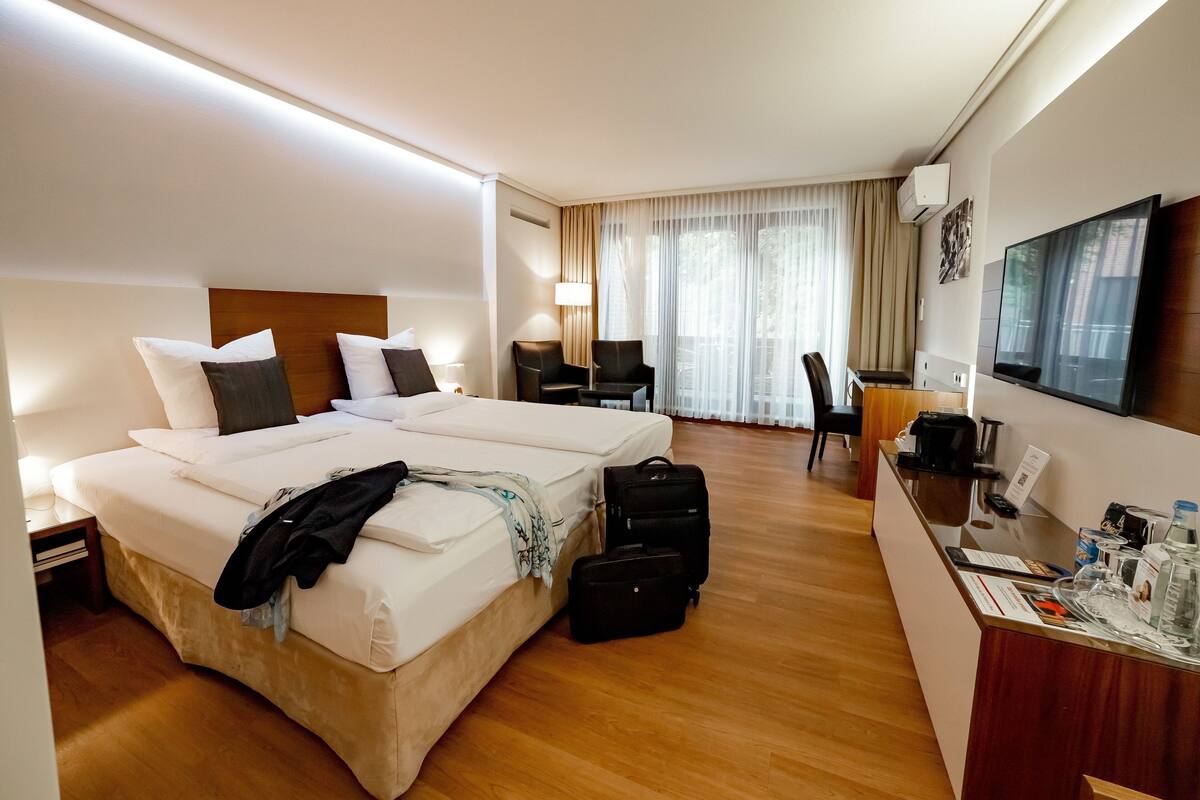 A hotel room with two beds, a desk, a TV, and a window with curtains.