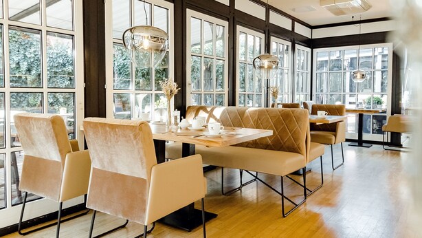 A spacious dining area with large windows, modern furniture, and pendant lighting. - Privathotel alte mühle (Weyhausen)