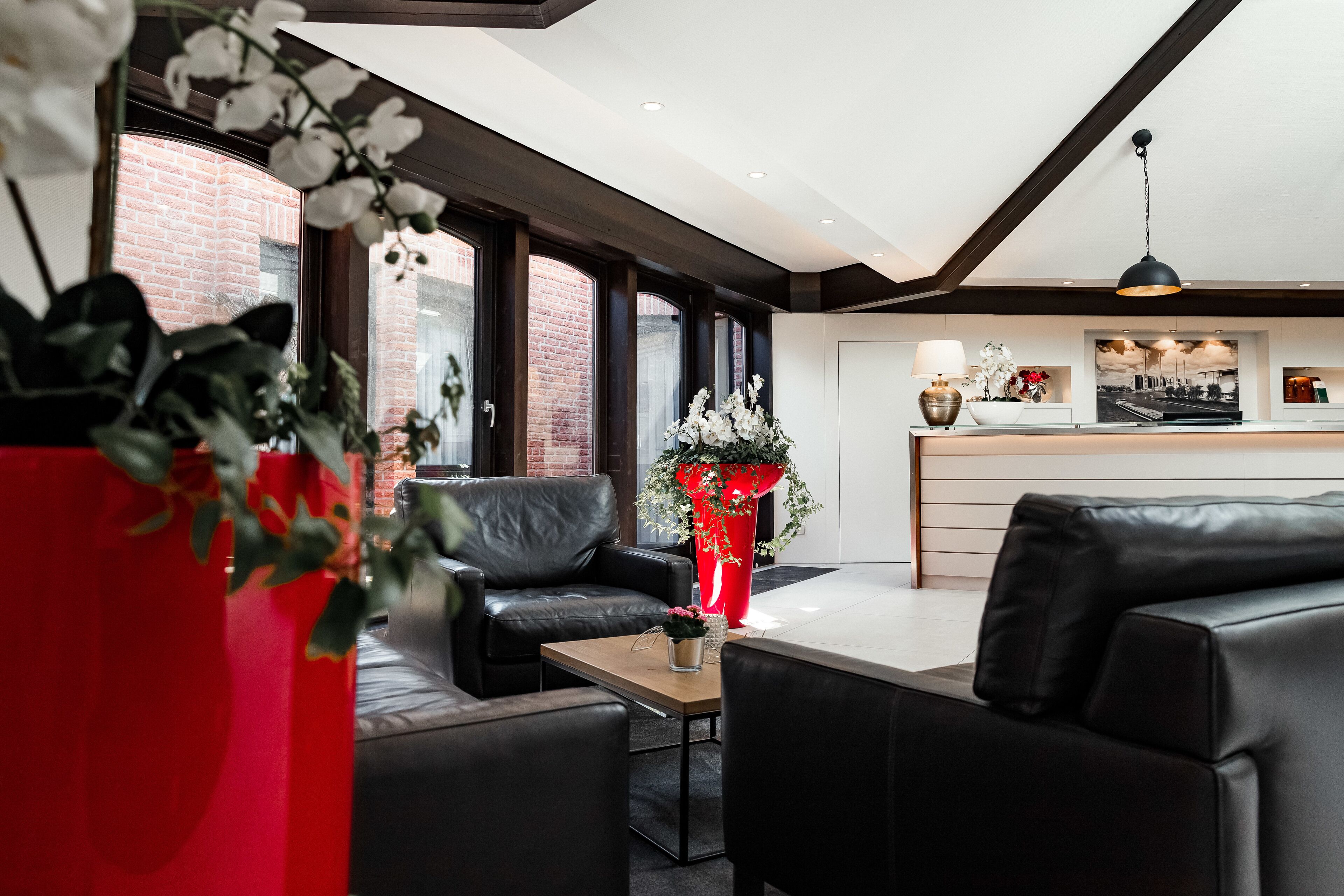 Een moderne woonkamer met leren banken, een houten salontafel en een rode vaas met bloemen.