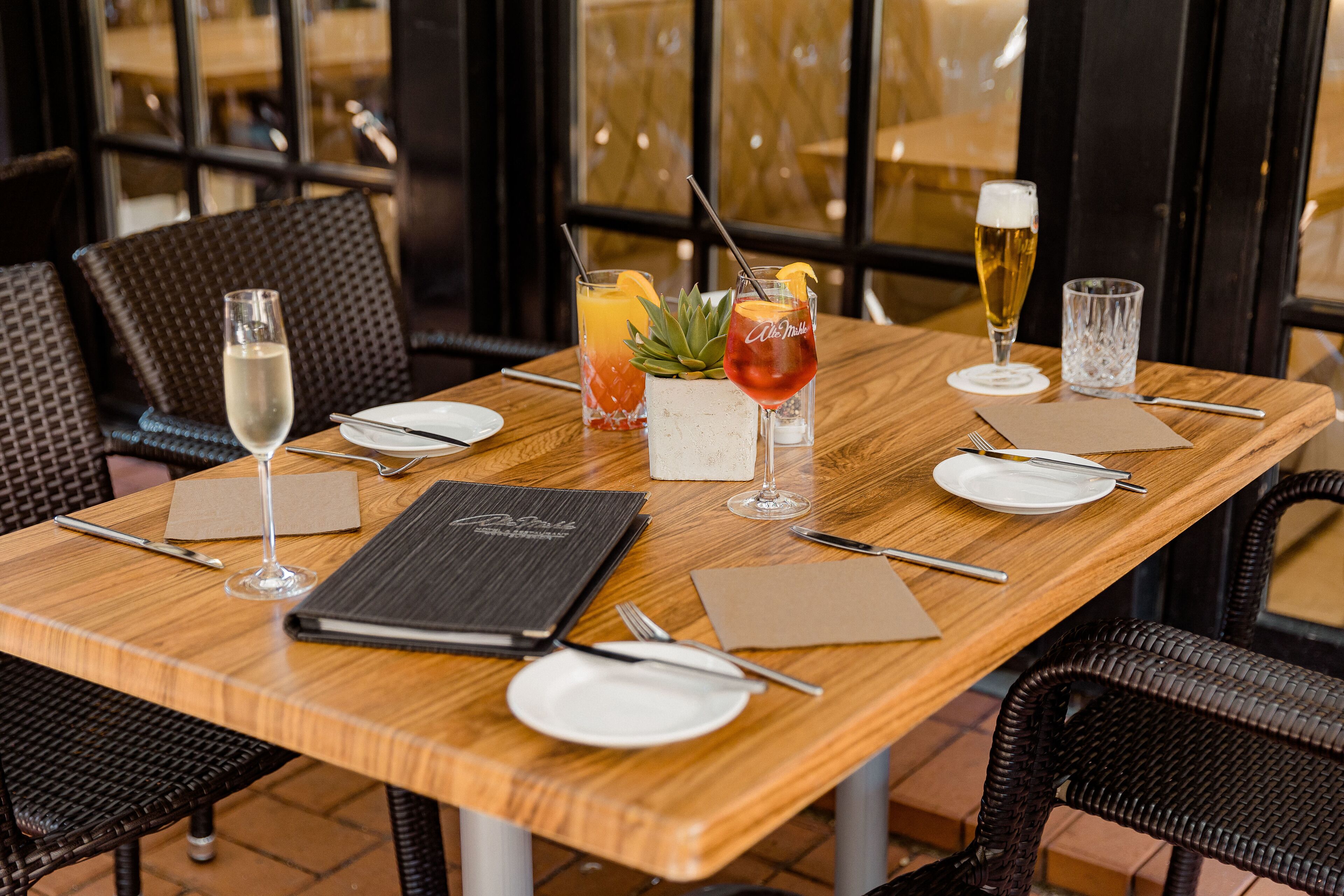 A restaurant table set with a menu, plates, cutlery, and various drinks.