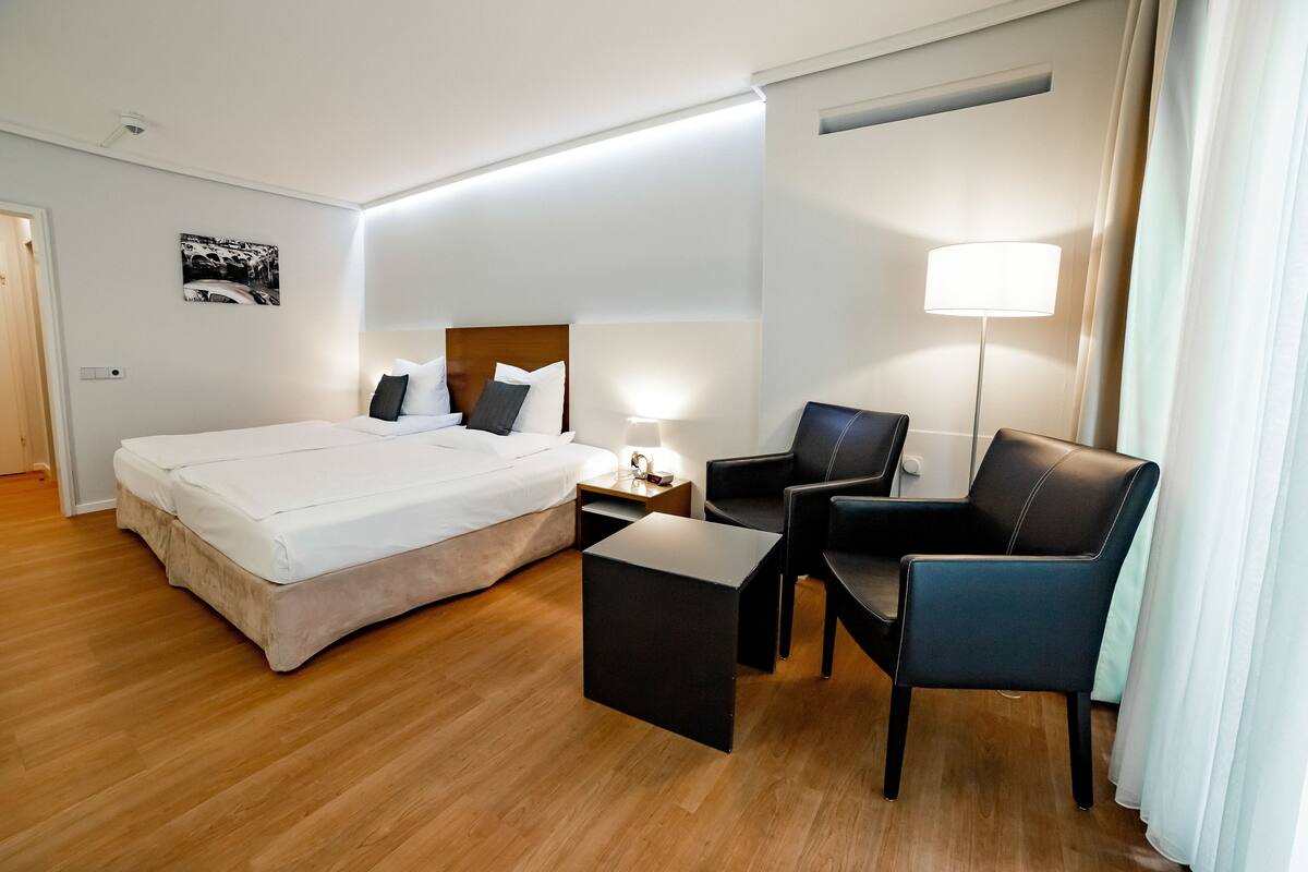 A hotel room with a bed, a desk, a chair, and a lamp.