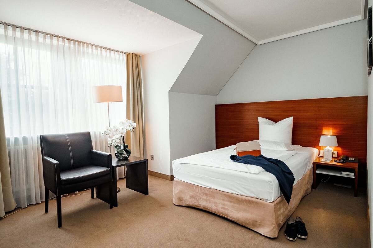A hotel room with a bed, a desk, a chair, a nightstand, and a lamp.