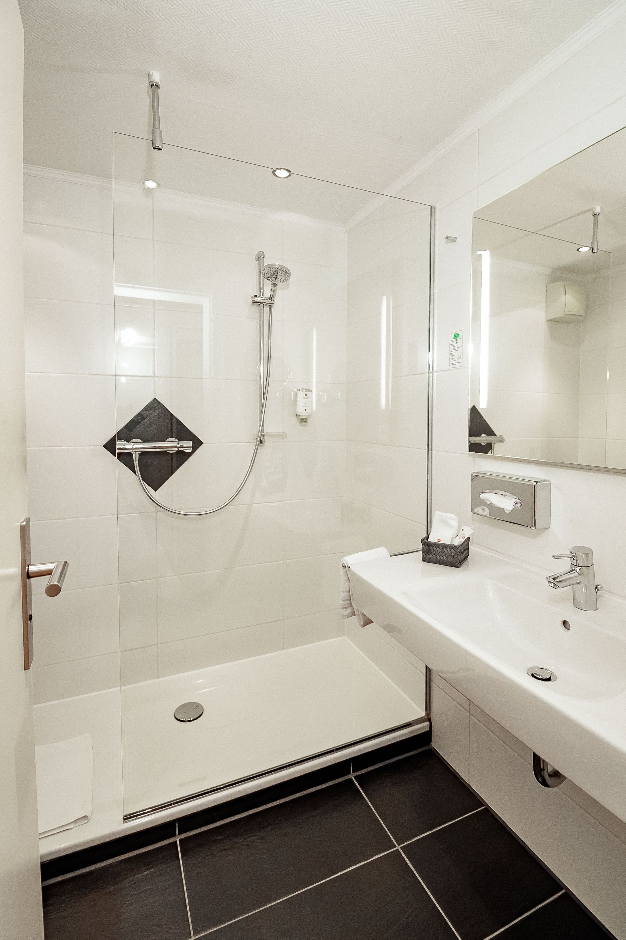 A modern bathroom with a glass-enclosed shower, a white sink, and a mirror.