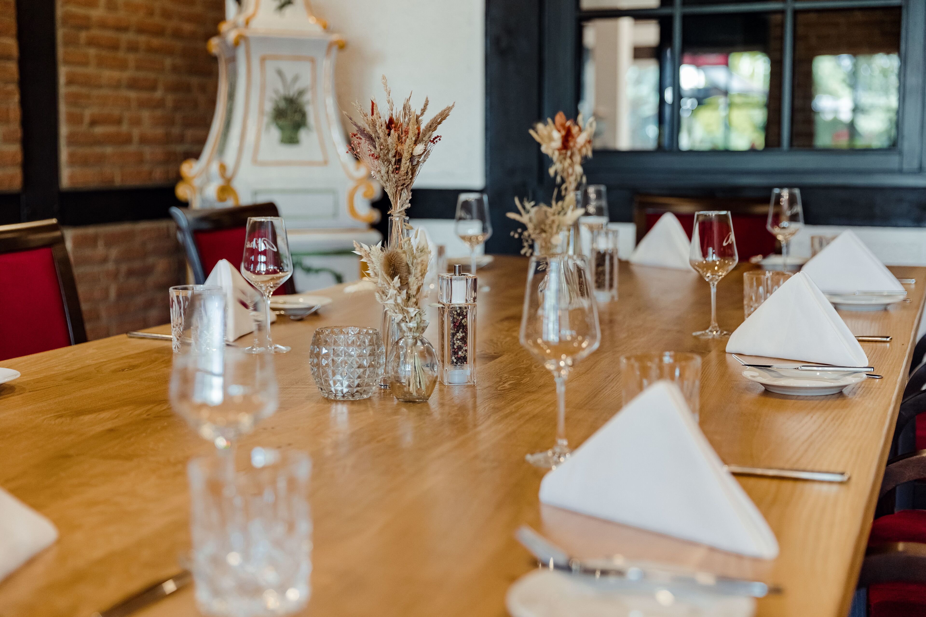 Une longue table à manger en bois, dressée avec des serviettes blanches, de la vaisselle transparente et des compositions florales décoratives.