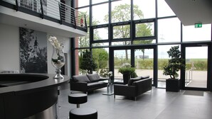 A modern lobby with a reception desk, black leather sofas, and large windows offering a view of the outdoors. - Privathotel alte mühle (Weyhausen)