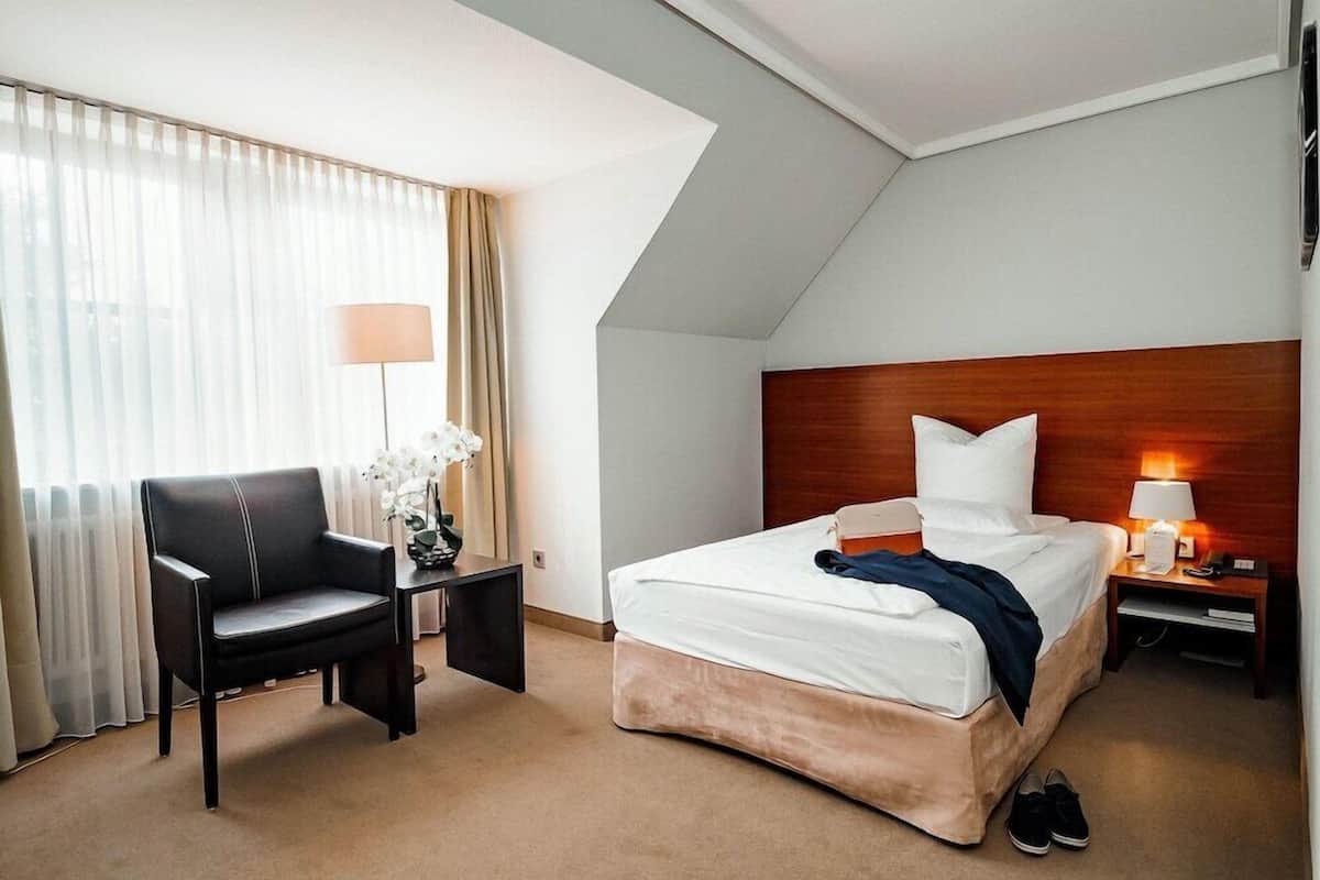 A hotel room with a bed, a desk, a chair, a lamp, and a window with curtains.