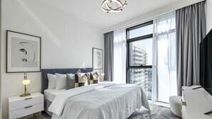 A modern hotel room with a large bed, a desk, and a view of the city through the window.