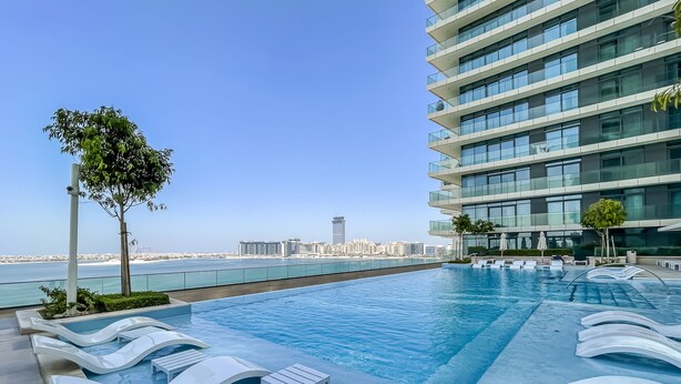 A rooftop swimming pool with lounge chairs and a view of the city skyline.