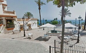 Ein Innenhof mit Außenbestuhlung, einer Fontäne und Blick aufs Meer.