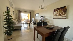 A living room with a sofa, a dining table with chairs, a TV, and a plant. - Estepona, well located apartment close to the beach and marina (Estepona)