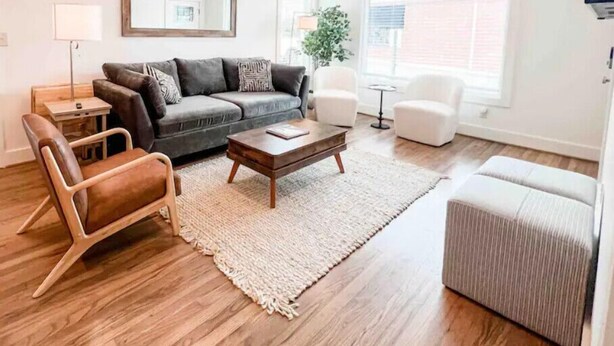 Un salon moderne avec un canapé gris, une table basse en bois et un fauteuil blanc.