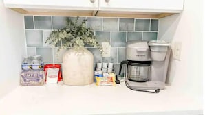 Un comptoir de cuisine avec une machine à café, un grand vase contenant des plantes vertes et divers produits alimentaires.