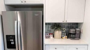 A kitchen with white cabinets, a stainless steel refrigerator, and a coffee maker on the countertop.