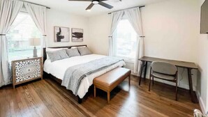 A bedroom with a bed, a desk, a chair, a ceiling fan, and a window with curtains.
