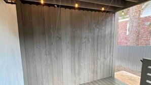 An outdoor patio area with a wooden deck, a covered section with a metal roof, and hanging lights. - Delightful 2 BR Condo Downtown Homewood (Birmingham)