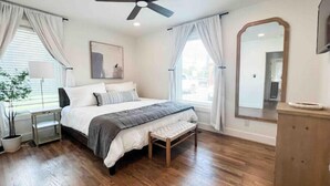 A bedroom with a bed, bedside tables, a ceiling fan, a mirror, and a window with curtains. - Delightful 2 BR Condo Downtown Homewood (Birmingham)