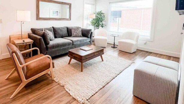 A modern living room with a grey sofa, a brown leather chair, a wooden coffee table, and a striped ottoman. - Delightful 2 BR Condo Downtown Homewood (Birmingham)