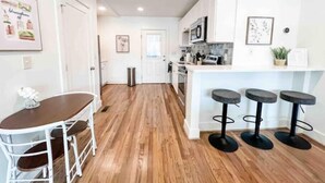 A modern kitchen with white cabinets, a wooden floor, a dining area with a white table and chairs, and a bar area with stools. - Delightful 2 BR Condo Downtown Homewood (Birmingham)