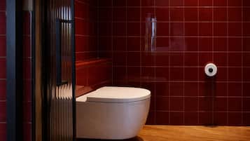 A modern bathroom with a white toilet, red tiled walls, and a wooden floor.