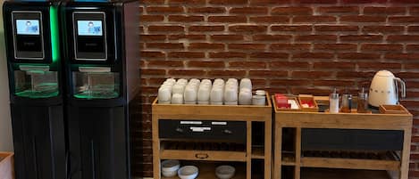 Una estación de café con dos máquinas de café, un expositor de madera con tazas y un hervidor en un carrito.