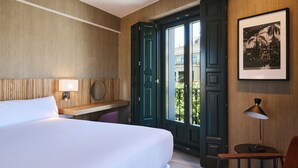 A hotel room with a bed, a desk with a lamp, a chair, and a door leading to an outdoor area. - Latroupe Prado (Madrid)