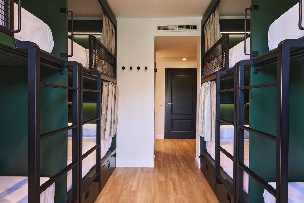 A corridor with bunk beds on either side, a door at the end, and a wooden floor.