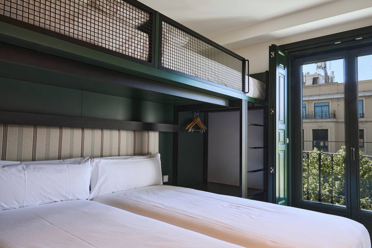 A hotel room with a large bed, a balcony with a view of buildings, and a hanging coat rack.