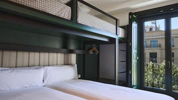 A hotel room with a large bed, a balcony with a view of buildings, and a hanging coat rack.