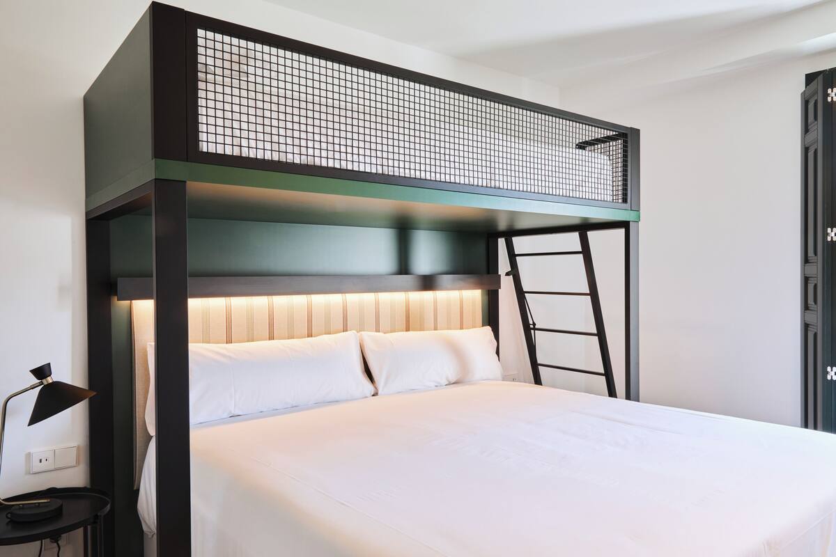 A bunk bed with a ladder, white bedding, and a wall-mounted light fixture.