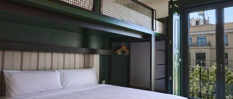 Un dormitorio con cama, perchero y balcón con vistas a edificios.
