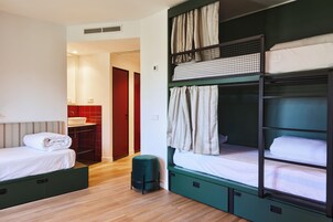 Una habitación tipo dormitorio con literas, un taburete pequeño y un baño con un lavabo rojo.