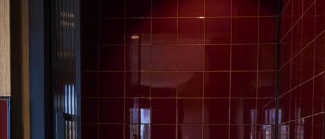 A modern bathroom with a large white bathtub, a wooden floor, and dark red tiled walls.