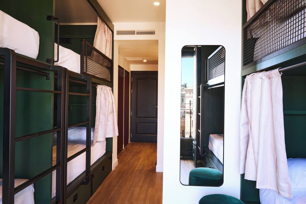 A dormitory-style room with bunk beds, a wooden floor, and a view through a window.