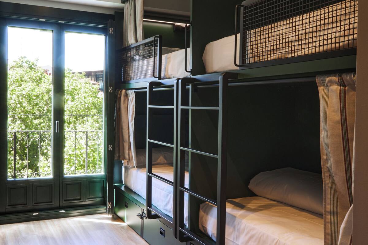 A bunk bed room with a wooden floor, a window with a view of trees, and a ceiling light.