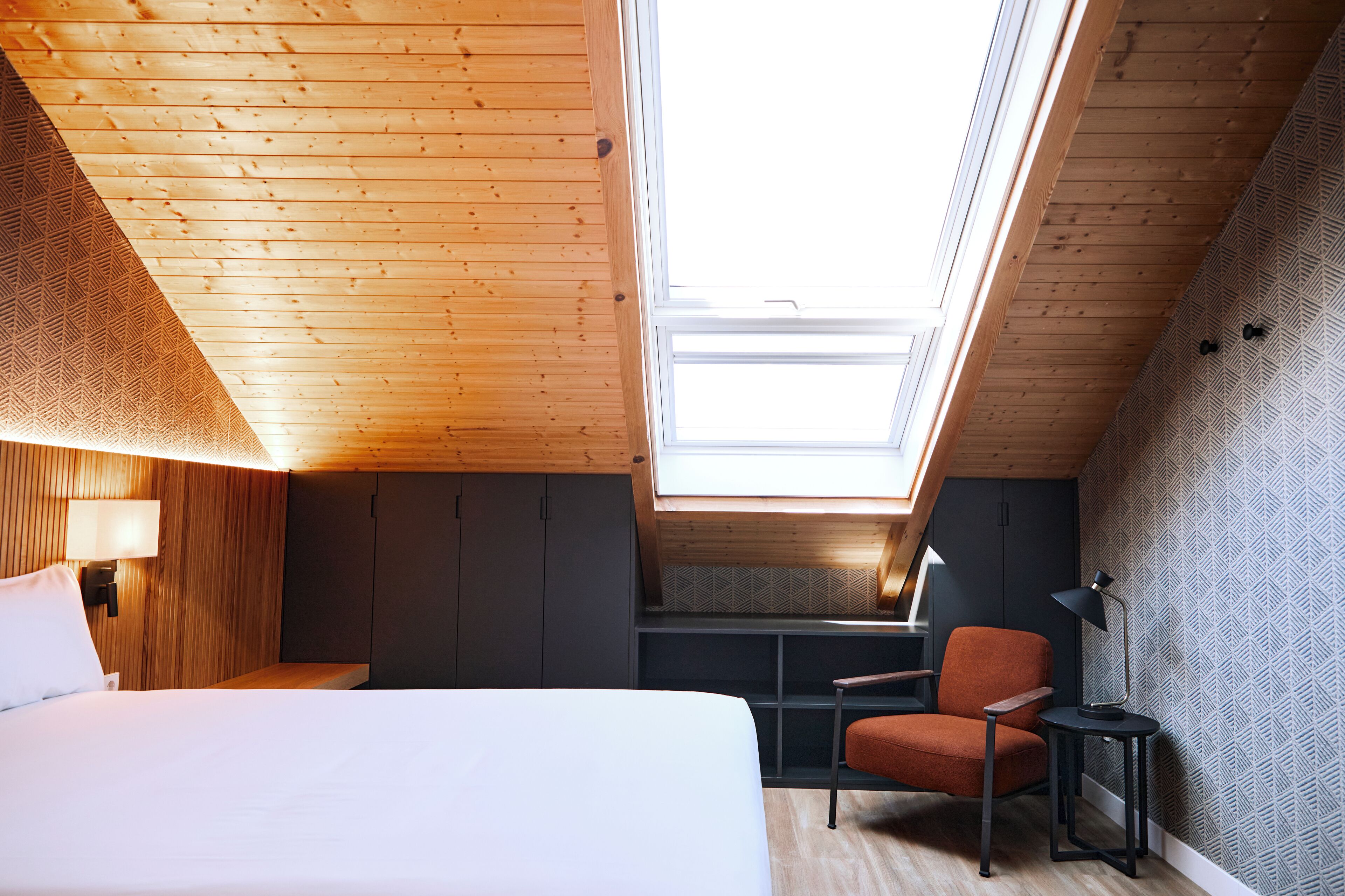 A modern bedroom with a skylight, a bed, a chair, and a desk.